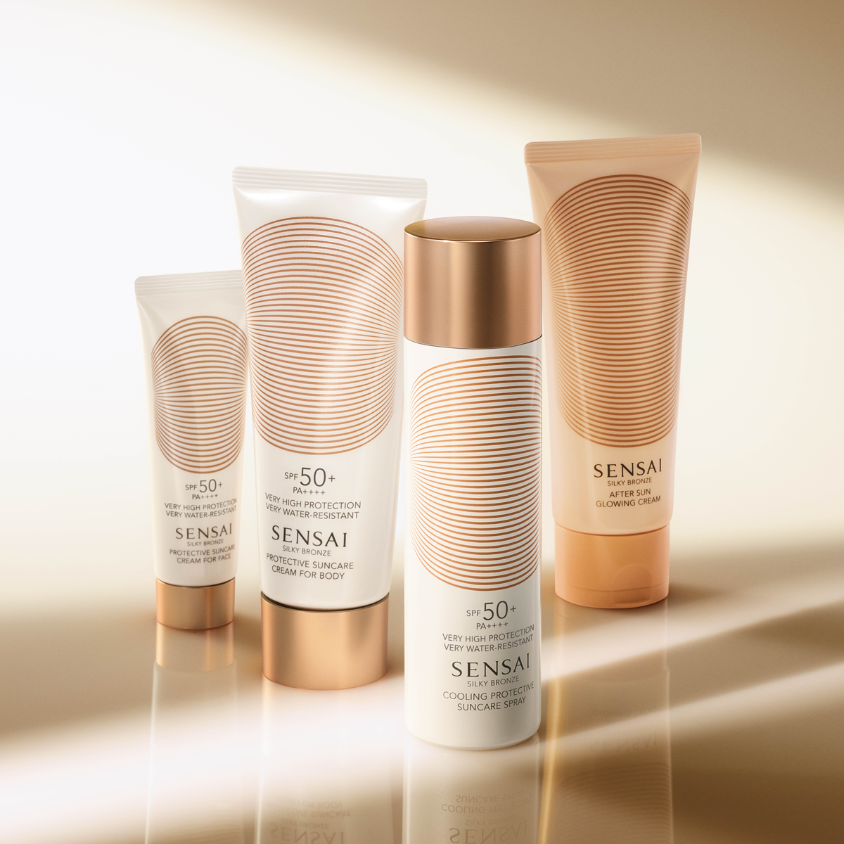 Neljä SENSAI Silky Bronze -aurinkosuojatuotetta esillä lämpimän beigen taustan edessä: Protective Suncare Cream for Face SPF 50+ PA++++, Protective Suncare Cream for Body SPF 50+ PA++++, Cooling Protective Suncare Spray SPF 50+ ja After Sun Glowing Cream. Tuotteissa on valkoinen ja kullanvärinen design, joka luo ylellisen vaikutelman premium sunscreen-, aurinkosuoja- ja after sun -tuotteista kasvoille ja vartalolle.