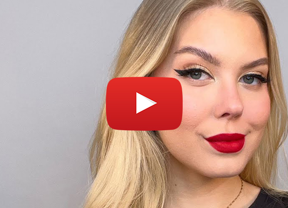 Henkilö, jolla on pitkät vaaleat hiukset, käyttää mustaa paitaa ja kultaketjua. Hänen edessään on punainen YouTube-painike.