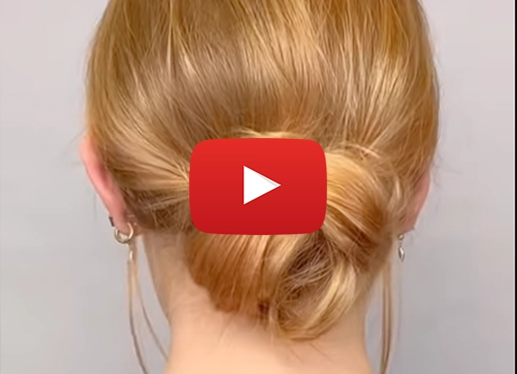 Henkilö, jolla on punaiset hiukset, on tehnyt tyylikkään hiussolmun ja seisoo neutraalin taustan edessä. Youtube play-merkki on sijoitettu kuvan keskelle.